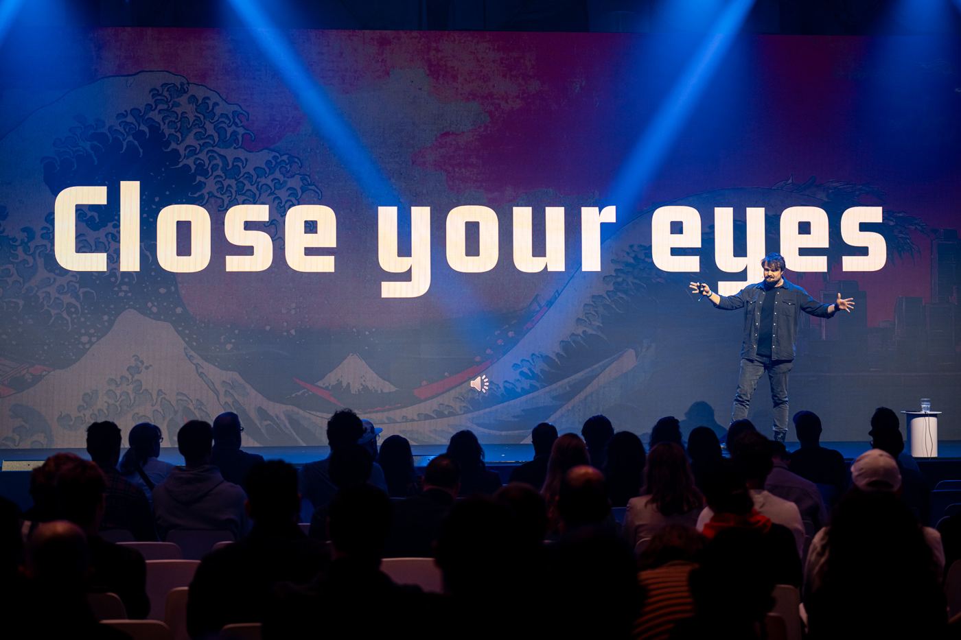 A darkened venue, the big screen reads: Close your eyes